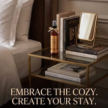 A styled bedroom scene with a bed, bedside table, books, a small mirror, and a bottle, with the text 'EMBRACE THE COZY. CREATE YOUR STAY.
