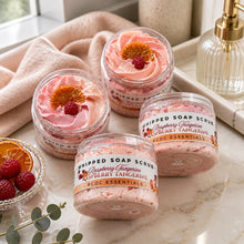 Jars of Raspberry Tangerine Whipped Soap Sugar Scrub with pink and orange hues, displayed alongside yellow tulips and decorative fruits on a white background.
