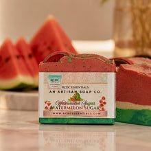 A bar of artisan soap labeled 'Watermelon Sugar' by RCDC Essentials, placed on a marble surface with watermelon slices blurred in the background.