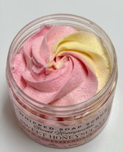 A clear plastic jar of whipped soap scrub with pink and pale yellow whipped cream-like swirls visible through the open top, labeled 'Whipped Soap Scrub' on the front.