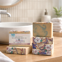 Stack of floral soap bars on a bathroom counter with 'An Artisan Soap Co.' branding.