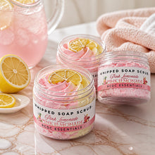 Jars of whipped soap sugar scrub with pink and yellow colors, alongside slices of lemon and pink flowers, indicating a citrus scent profile.