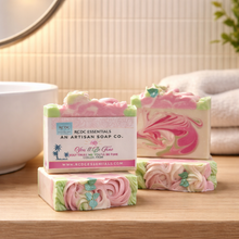 Three bars of soap with a pink and green design on a wooden surface, featuring RDC Essentials branding.