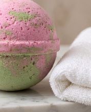 A close-up of a pink and green marbled bath bomb next to a folded white towel on a marble surface.
