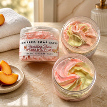 Jars of Sparkling Peach Whipped Soap Sugar Scrub, with a pink and white color scheme, displayed on a white surface with a bouquet of pink flowers in the background.