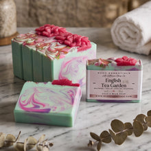 Handmade soap bars and a wrapped bar of soap from MCDC Essentials 'The Garden Soaps Co' labeled 'English Tea Garden', styled on a marble surface with eucalyptus leaves and a rolled towel in the background.