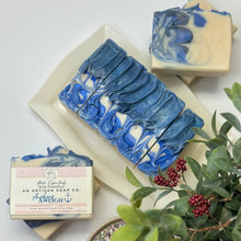 Handmade cold process soap bar with swirled blue and gray colors, placed on a white dish, with a label in the foreground.