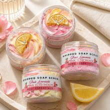 Jars of whipped soap sugar scrub with pink and yellow colors, alongside slices of lemon and pink flowers, indicating a citrus scent profile.