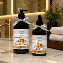 Two amber glass pump and dropper bottles of RCDC Essentials Shower Gel & Body Wash in Amber Noir, styled on a marble bathroom counter with a gold faucet, white towels, and a plant in the background.
