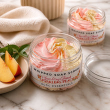Jars of Sparkling Peach Whipped Soap Sugar Scrub, with a pink and white color scheme, displayed on a white surface with a bouquet of pink flowers in the background.