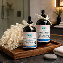 Two bottles of 'Confidence' shower gel and body wash on a wooden tray with a loofah and bath towel in a bathroom setting.