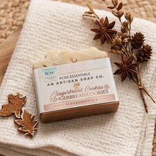 A bar of RCDC Essentials Gingerbread Cookies soap bar, wrapped in a kraft paper sleeve, displayed on a textured cream towel with dried botanicals and star anise.