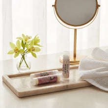 Lip balms on a marble tray with a mirror and flowers in the background