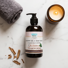 Bottle of shower gel & body wash with teakwood scent on a marble surface with a candle and towel.