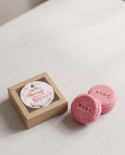 Two pink round solid shampoo bar with embossed 'RCDC' logos next to a small kraft paper gift box with a round floral label reading 'Rose & Bloom'.