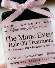 A close-up of a black bottle of RCDC Essentials 'The Mane Event' Hair Oil Treatment, wrapped with a light pink ribbon and bow with a pearl accent, showing the product label.