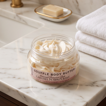 A jar of Kiehl's Saffrole Body Butter in Caramel Pumpkin Bake scent, filled with whipped cream-colored butter, set on a white marble bathroom counter with a folded white towel and gold faucet in the background.