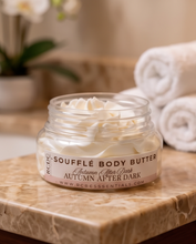 A jar of RCDC Soufflé Body Butter, Autumn After Dark, filled with whipped cream-colored body butter and resting on a marble tray with rolled towels in the background.