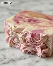 A close-up of a swirled handmade soap bar with pink and cream layers and small red berry inclusions, resting on a light marble surface. The text 'Panel 2' appears in the top-left corner.