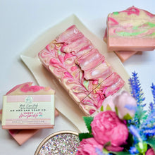A bar of handmade soap with a pink and green marbled pattern, displayed alongside a box with the brand name 'Hey Delilah' and decorative flowers.