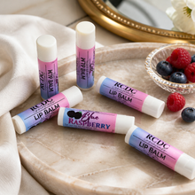 RCDC lip balms on a marble surface with berries and a mirror in the background